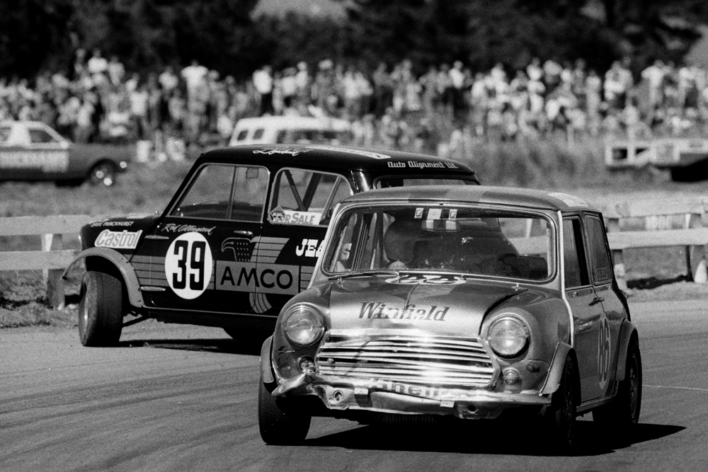 BayPark 1972. BNSW 1000 cc Mini days. Barrie Philips pass the crashed car of champion Rod Collingwood. IMAGE/terry marshall